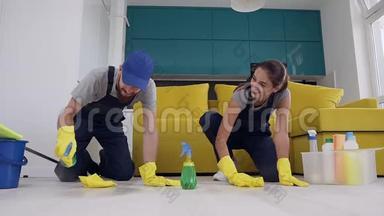 清洁公司有魅力的男人和女人在木地板上喷洒<strong>清洁剂</strong>，用抹布擦拭